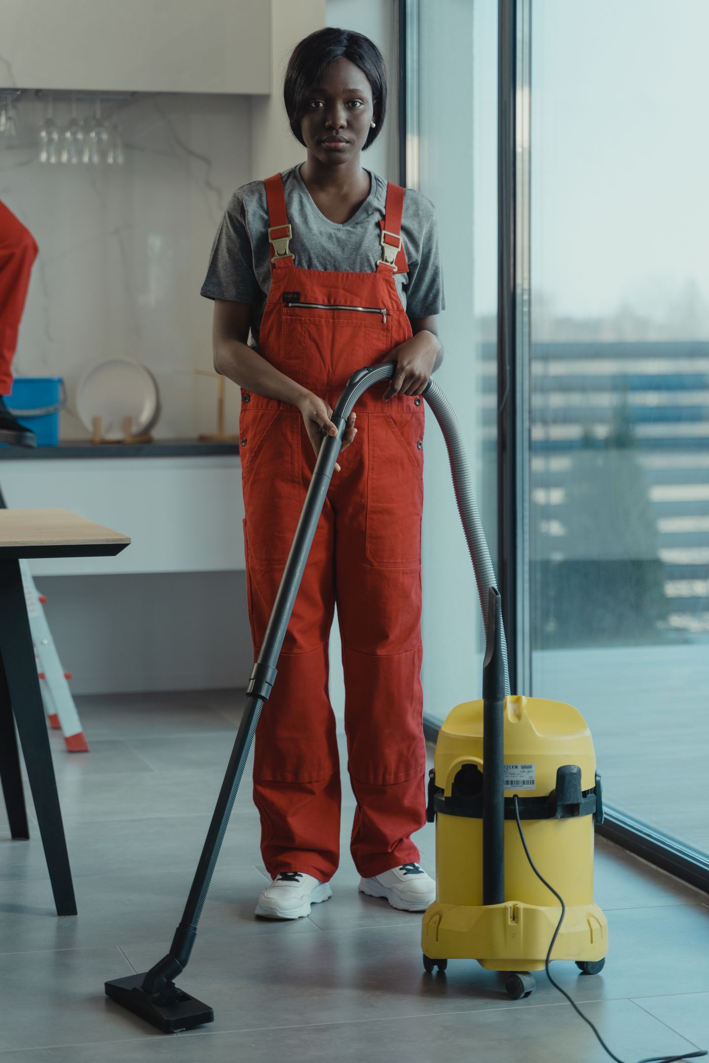 Crew member vacuuming a bright common area beside floor-to-ceiling windows